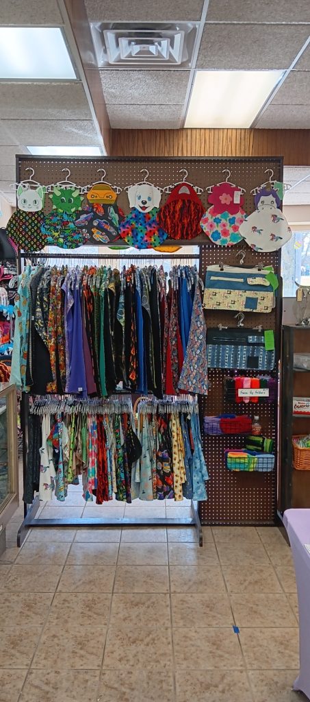 Two hanging racks with clothing items, display has homemade items, bibs, etc.
