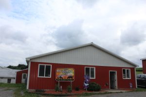 Barn with three windows and an open door. White siding on the triangle top and red siding to make a rectangle. Sign reads My Bar K Meadow's The Smith Family
